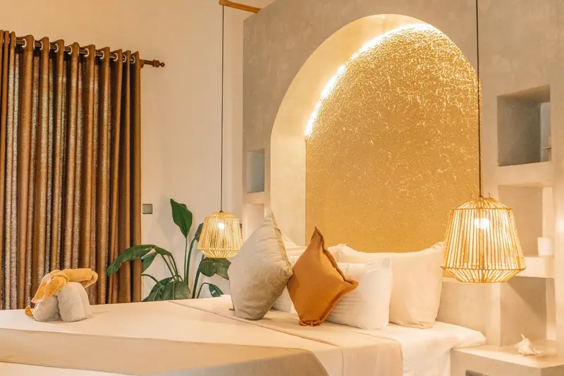 Glowing arched headboard, linen cushions and rattan lamps beside the bed