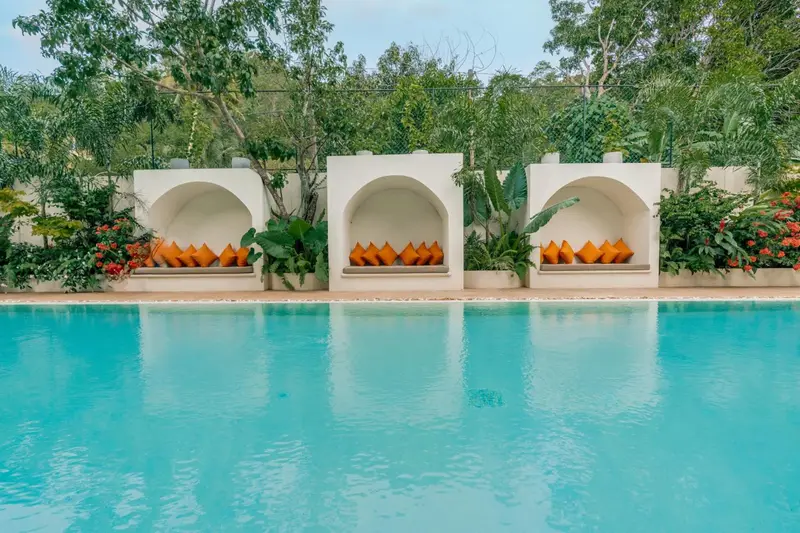 Three white arched cabanas with orange cushions beside the turquoise pool
