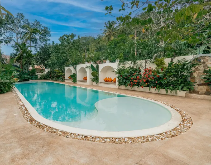 The pool's sandy shallow end, cabanas and jungle greenery under blue sky