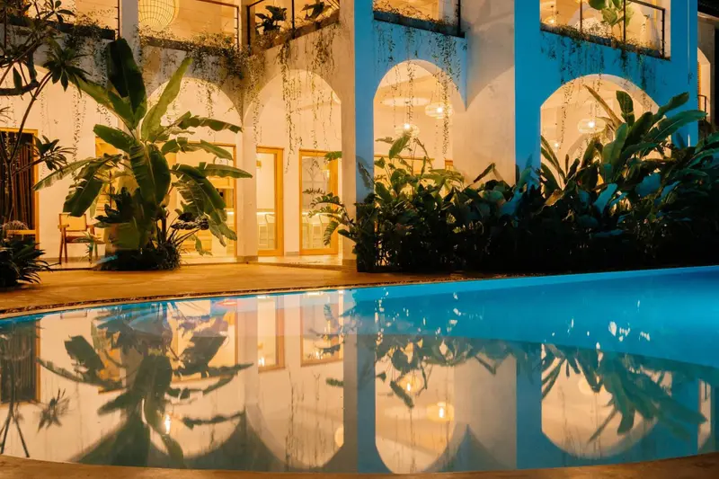 Warm lights of the villa reflected in the pool at dusk