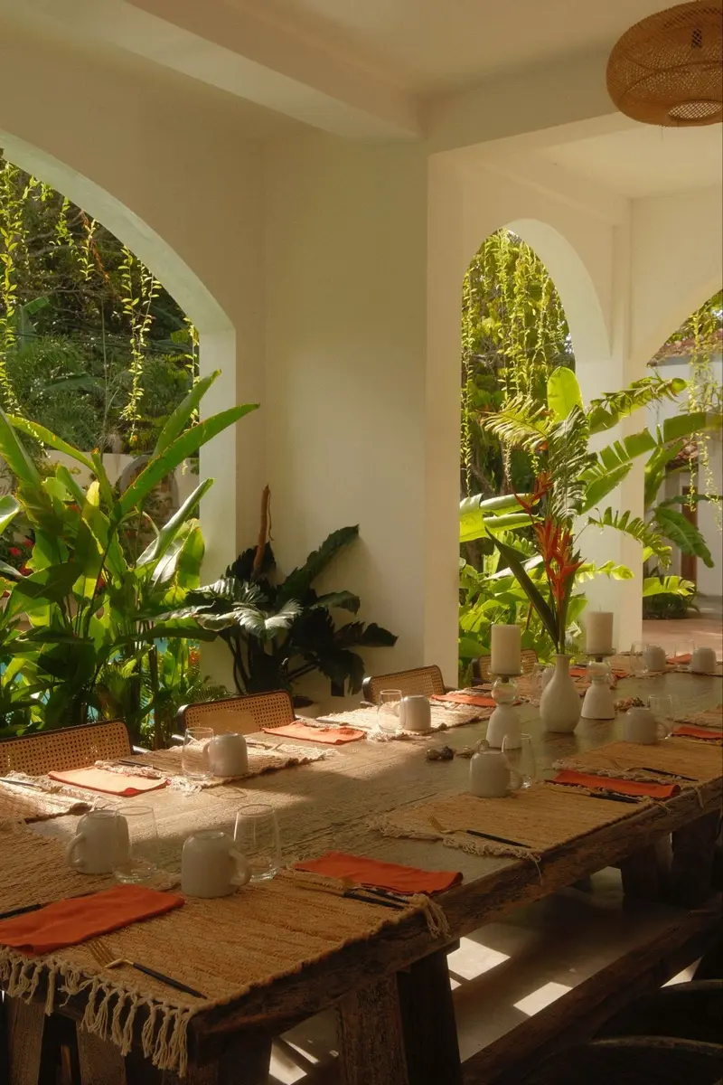 Breakfast table laid with woven mats and orange napkins under garden arches