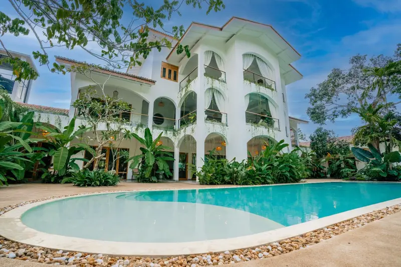 Three-storey white villa with arched balconies behind the curved pool