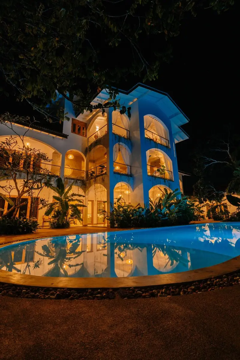 The villa lit up at night above the glowing pool